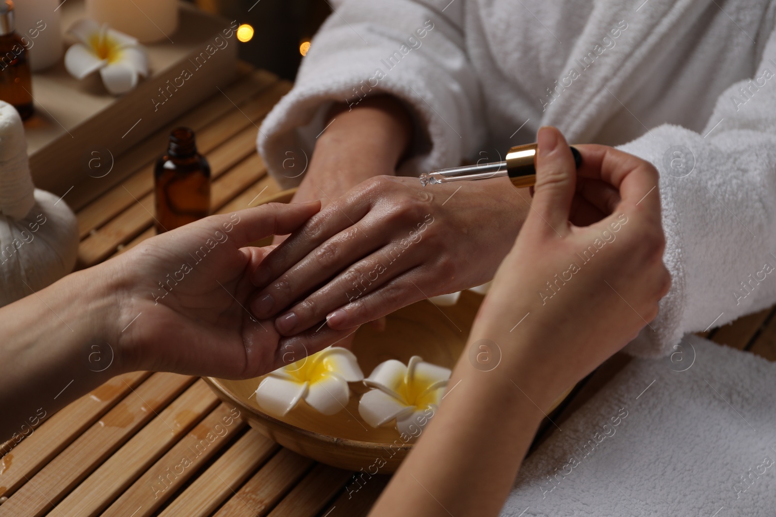 Photo of Woman receiving hand treatment at wooden table in spa, closeup