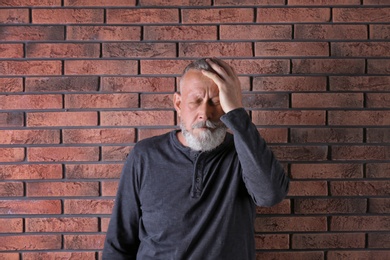 Photo of Senior man in state of depression near brick wall