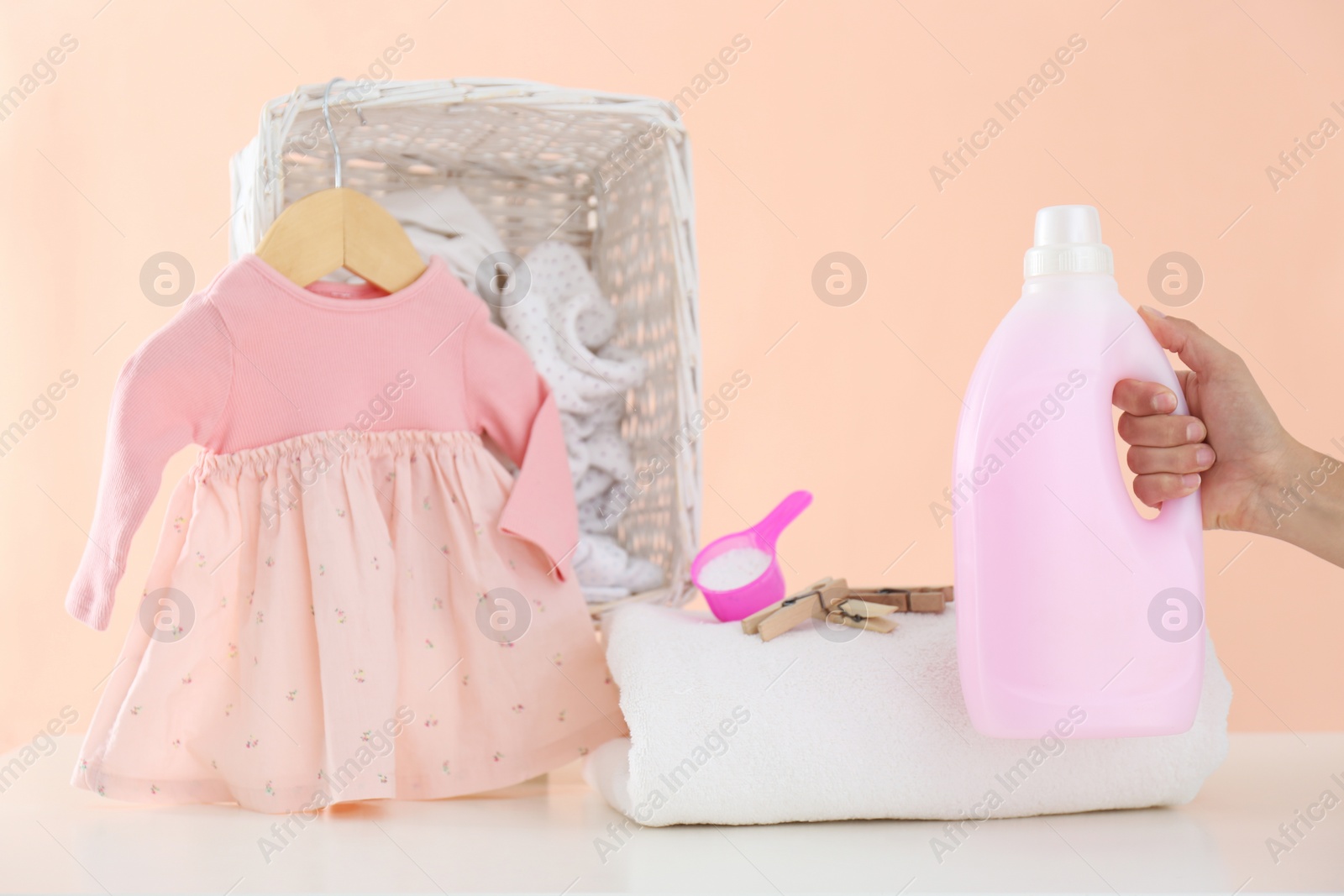 Photo of Woman with detergent and children's clothes at white table, closeup