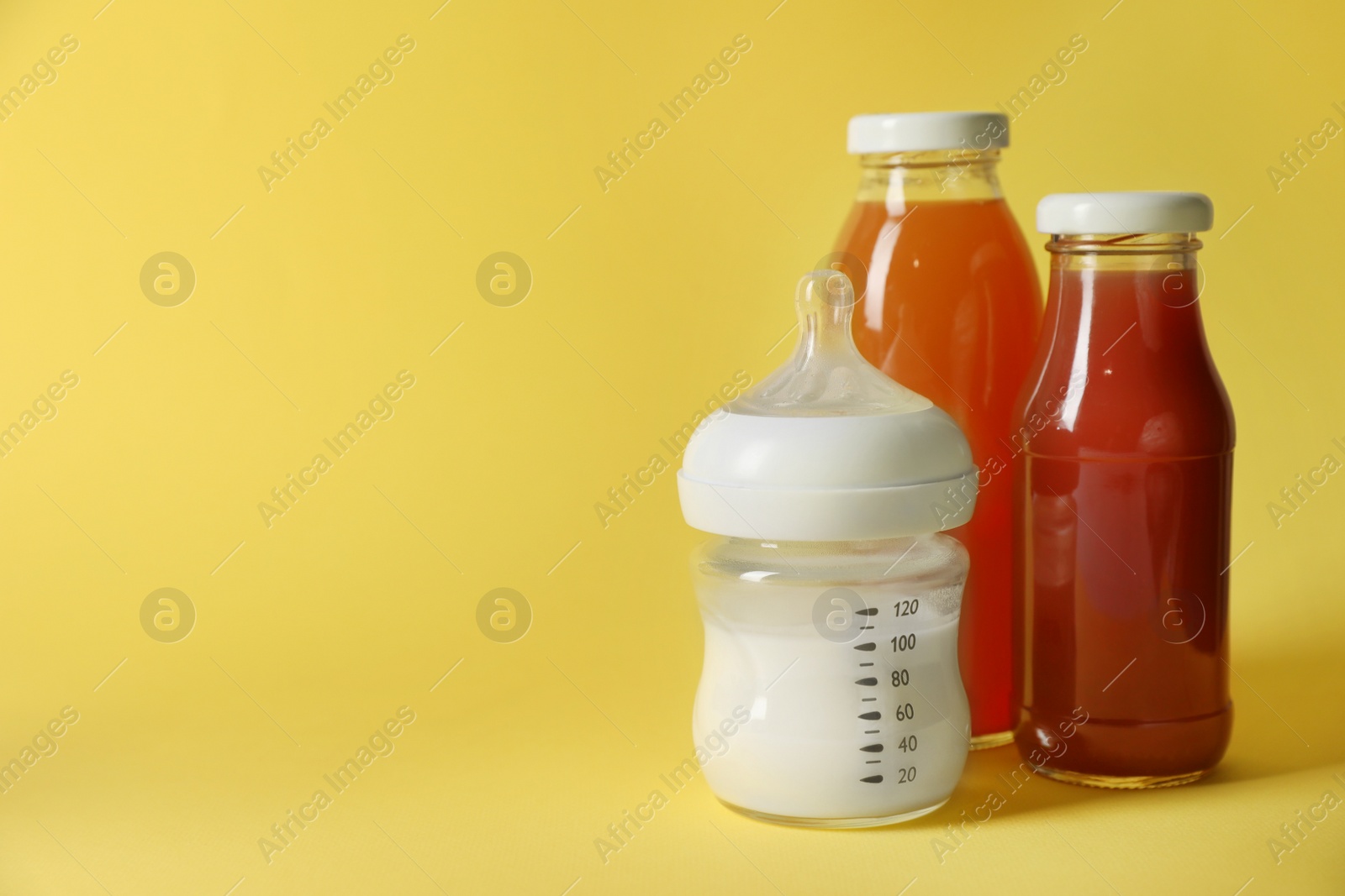 Photo of Bottles with milk and juice on yellow background, space for text