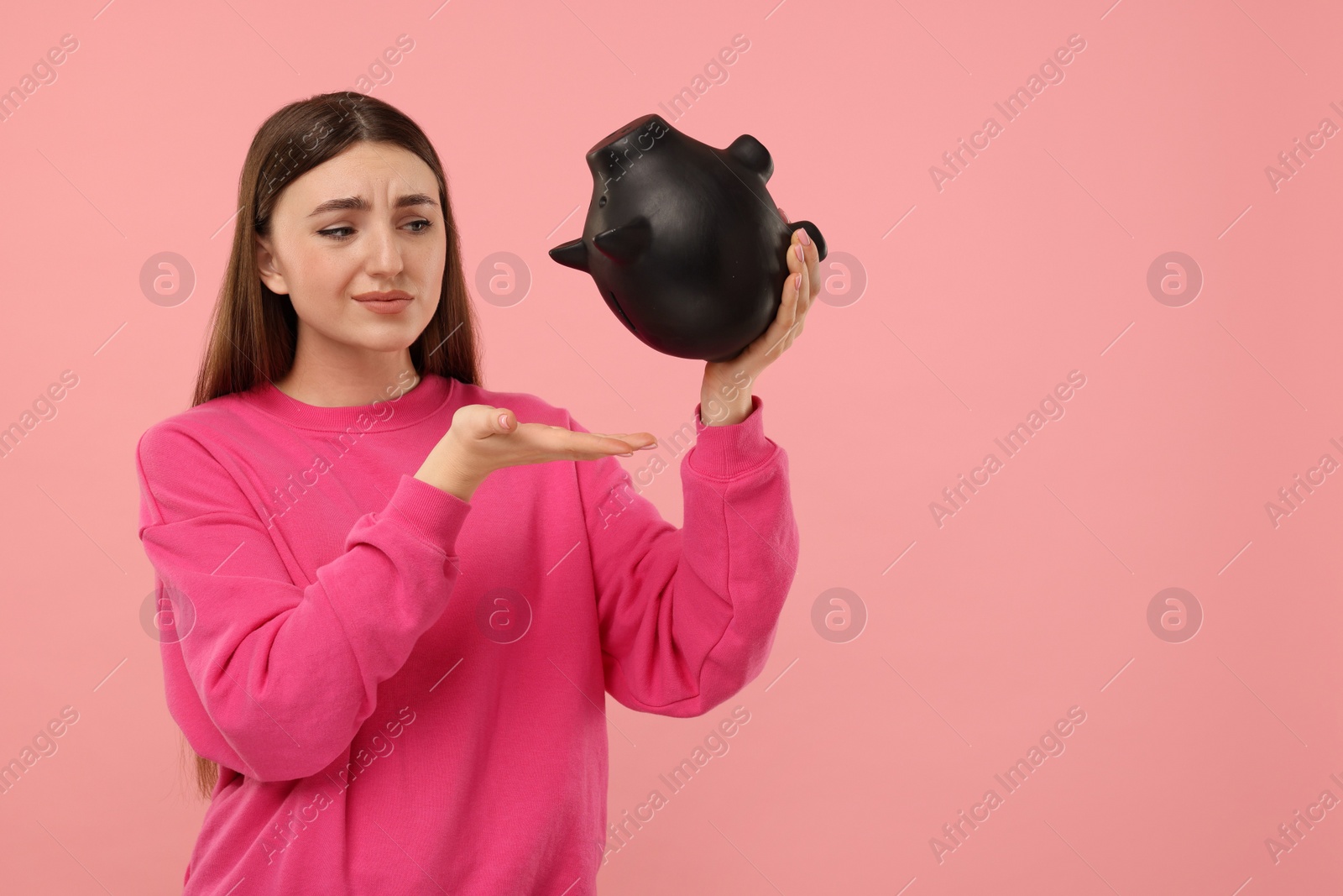 Photo of Sad woman with piggy bank on pink background, space for text