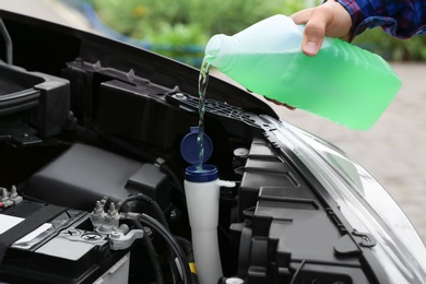 Photo of Man pouring liquid from plastic canister into car washer fluid reservoir, closeup