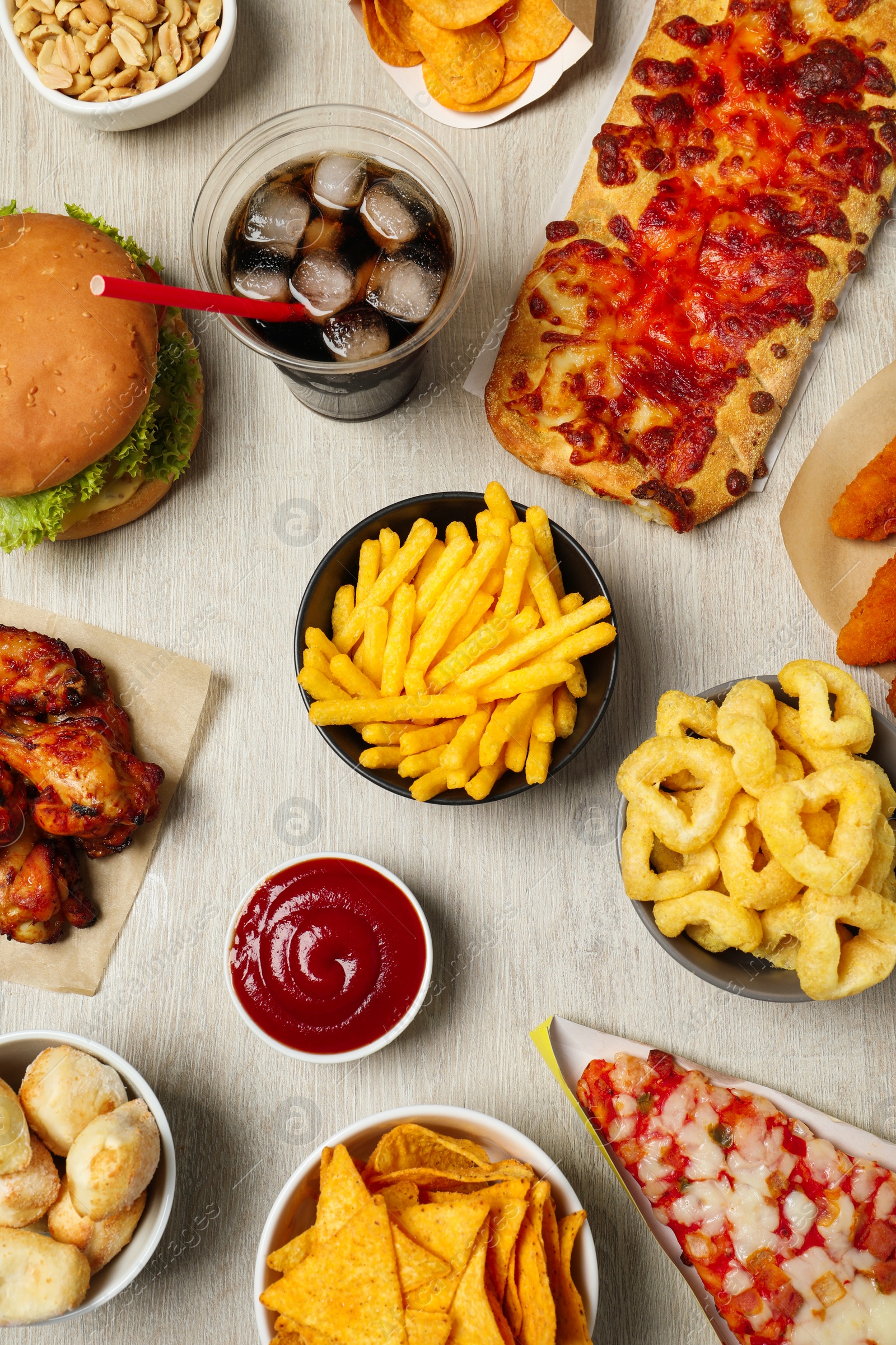 Photo of French fries, onion rings and other fast food on white wooden table, flat lay