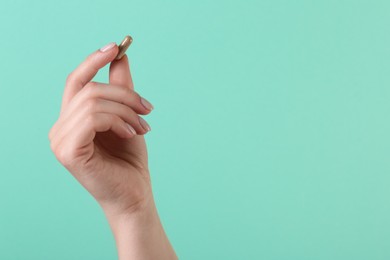 Photo of Woman holding vitamin capsule on turquoise background, closeup with space for text. Health supplement