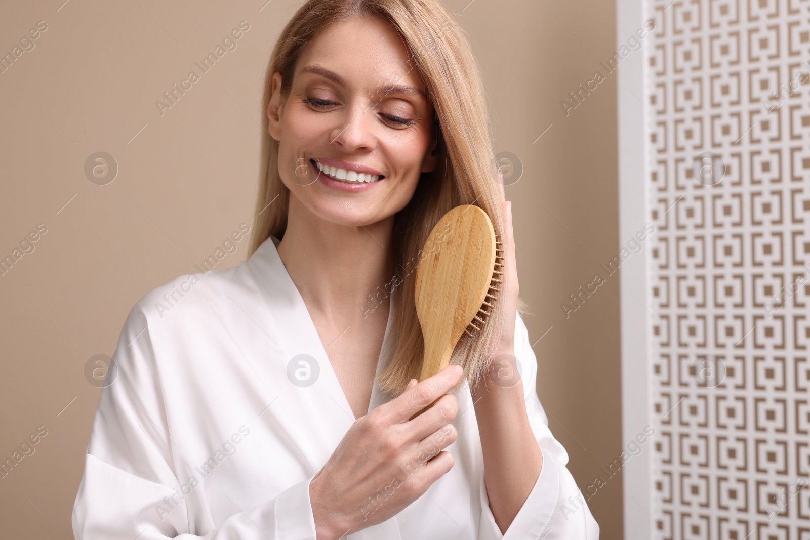 Photo of Beautiful woman in white robe brushing her hair indoors