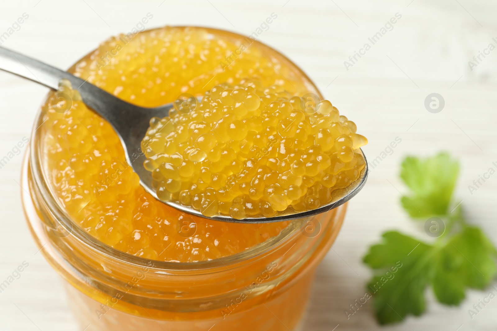 Photo of Taking fresh pike caviar from glass jar on white wooden table, closeup