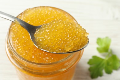 Taking fresh pike caviar from glass jar on white wooden table, closeup