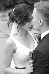 Photo of Happy newlyweds kissing outdoors, black and white effect