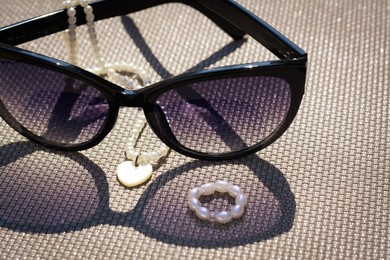 Stylish sunglasses and jewelry on grey surface, closeup