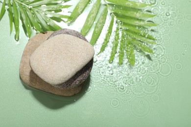 Photo of Spa stones and palm leaves in water on light green background, flat lay. Space for text