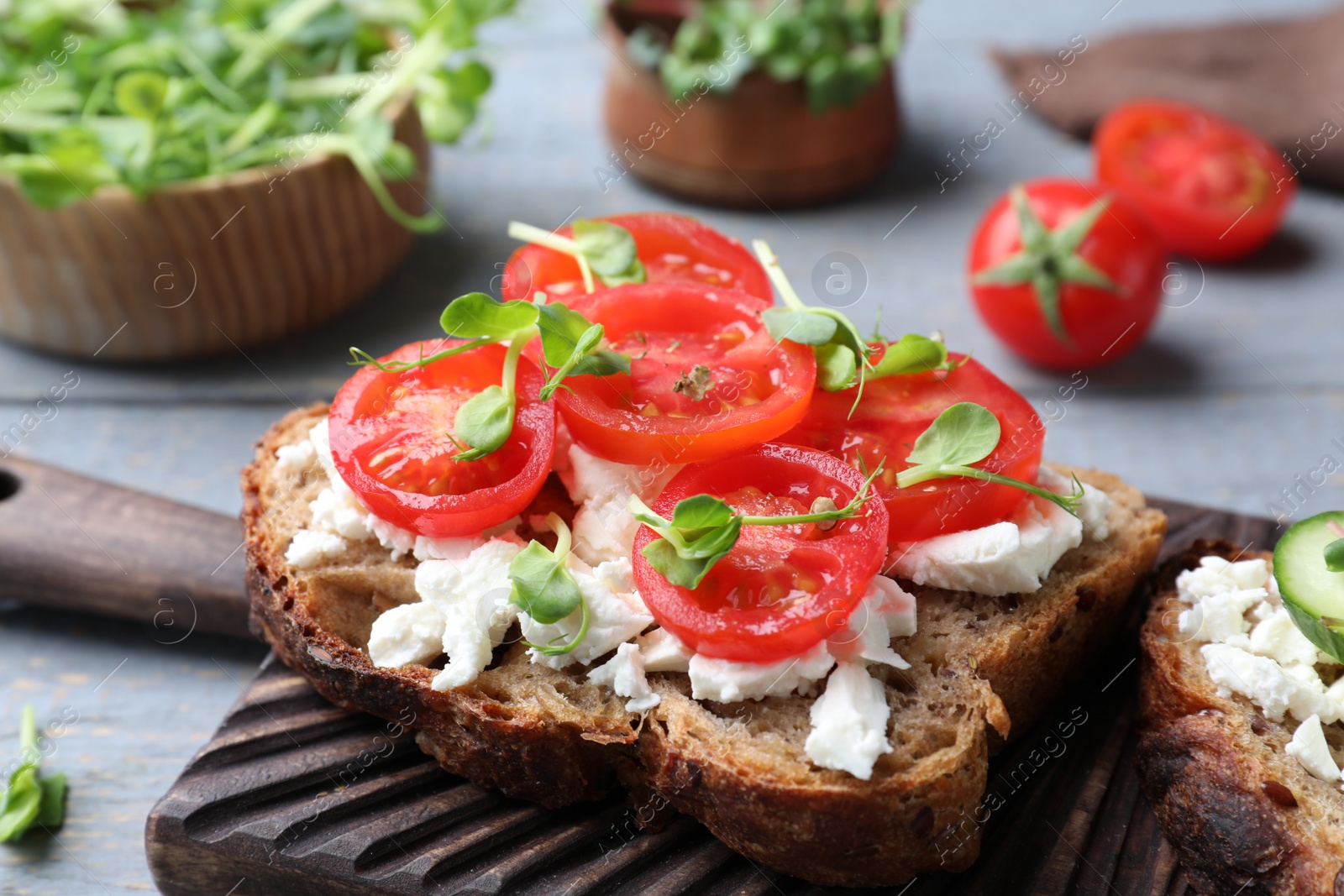 Photo of Delicious sandwich with cherry tomatoes, microgreens and cheese on wooden board, closeup