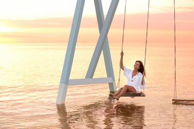 Young woman enjoying sunrise on swing over water