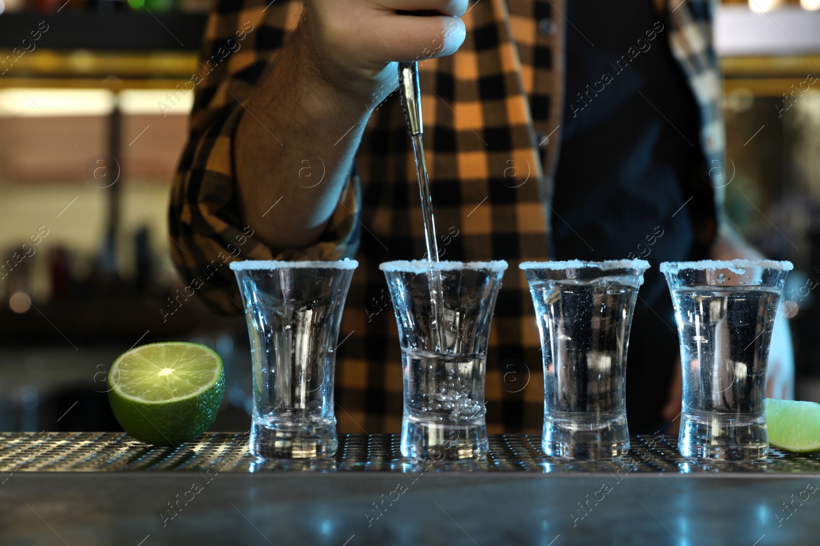 Photo of Bartender pouring Mexican Tequila into shot glasses at bar counter, closeup