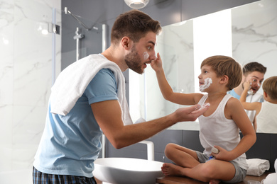 Photo of Dad and son with shaving foam on their faces having fun in bathroom