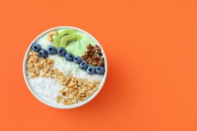 Photo of Tasty smoothie bowl with fresh kiwi fruit, blueberries and oatmeal on orange background, top view. Space for text