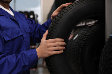 Photo of Male mechanic with car tire in auto store, closeup