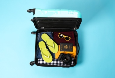 Open suitcase with traveler's belongings on color background, top view