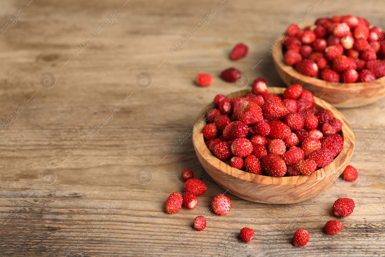 Photo of Fresh wild strawberries in bowls on wooden table. Space for text