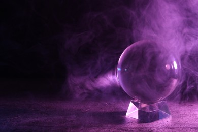Photo of Crystal ball on table and smoke against dark background, space for text. Predictions of future
