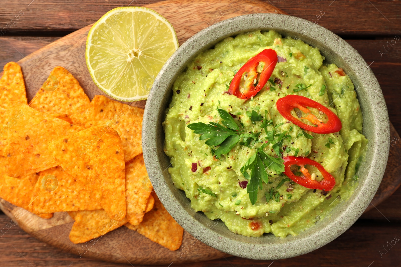 Photo of Bowl of delicious guacamole, lime and nachos chips on wooden table, top view