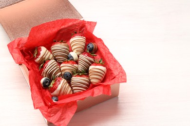 Photo of Box with delicious chocolate covered strawberries and blueberries on white table. Space for text