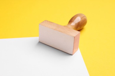 Photo of One wooden stamp tool and sheet of paper on yellow background, closeup