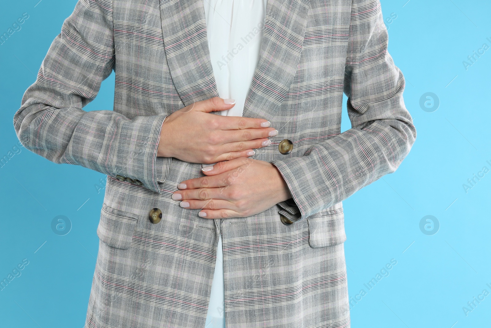 Photo of Woman in office suit suffering from stomach ache on light blue background, closeup. Food poisoning