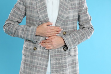 Woman in office suit suffering from stomach ache on light blue background, closeup. Food poisoning