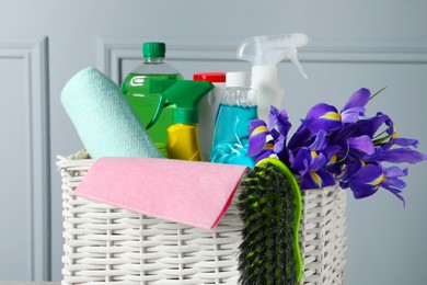 Photo of Spring cleaning. Basket with detergents, flowers and tools near grey wall, closeup