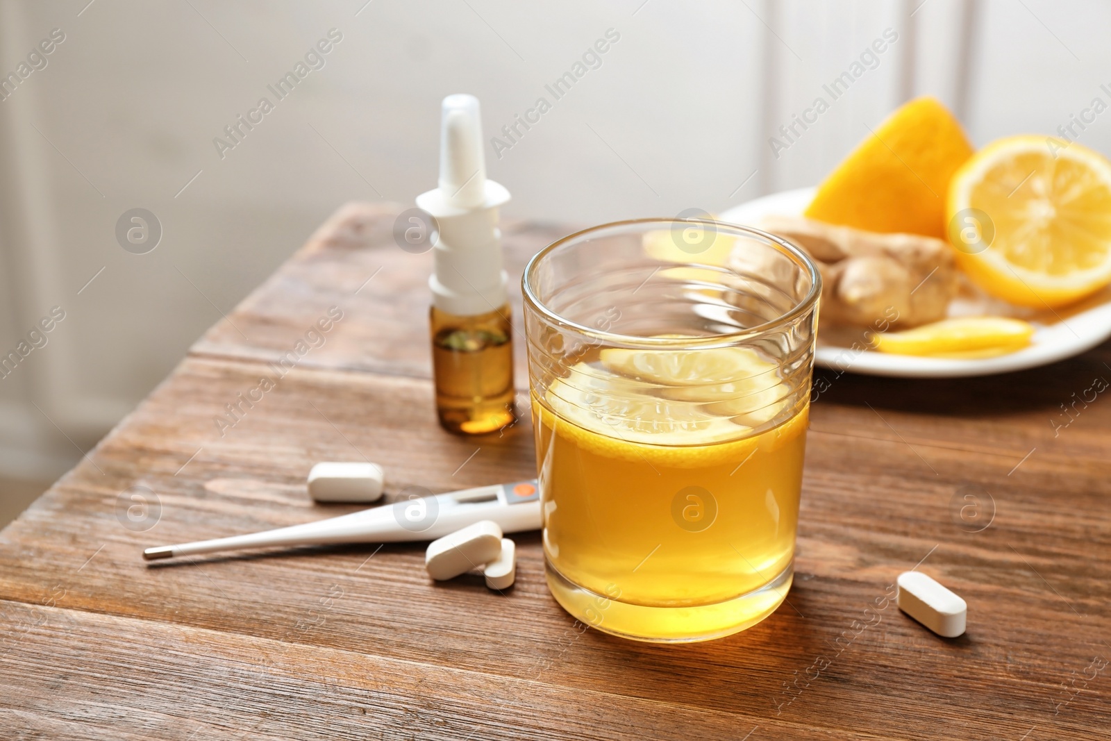 Photo of Glass with hot tea, lemon and pills for cold on wooden table