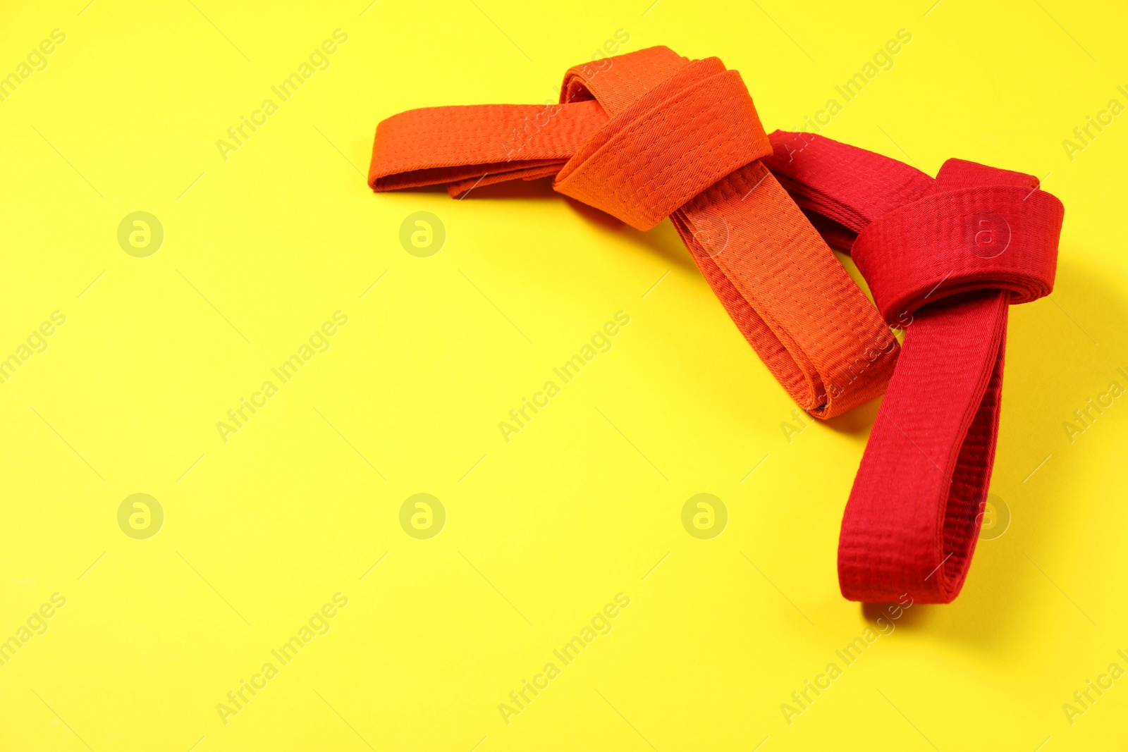 Photo of Red and orange karate belts on yellow background, space for text