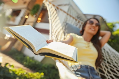 Photo of Young woman resting in hammock near motorhome outdoors, focus on book