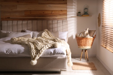 Photo of Bed with white knitted plaid in room. Interior design