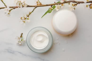 Photo of Flat lay composition with jars of face cream and flowers on white marble table