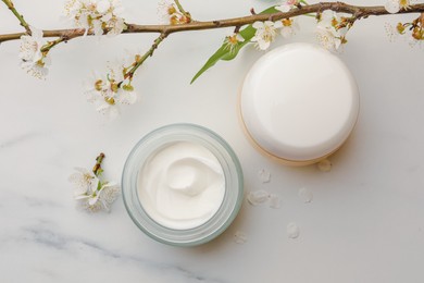 Flat lay composition with jars of face cream and flowers on white marble table