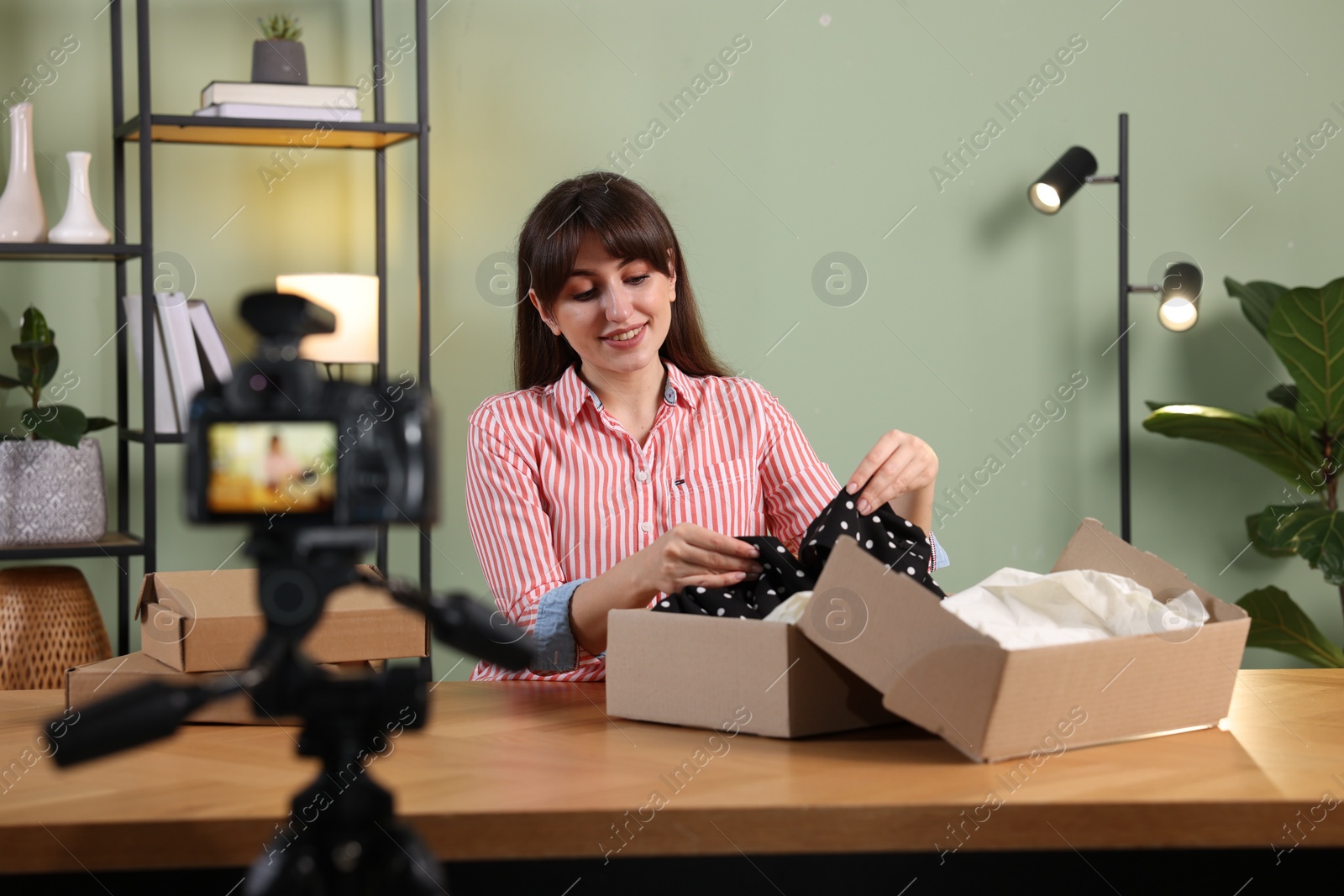 Photo of Smiling fashion blogger recording video while talking about clothes at home