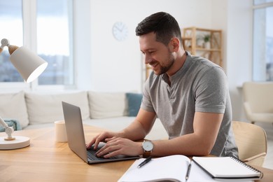 Photo of Happy man working on laptop at wooden desk in room