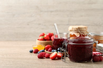 Jars with different jams and fresh fruits on wooden table. Space for text