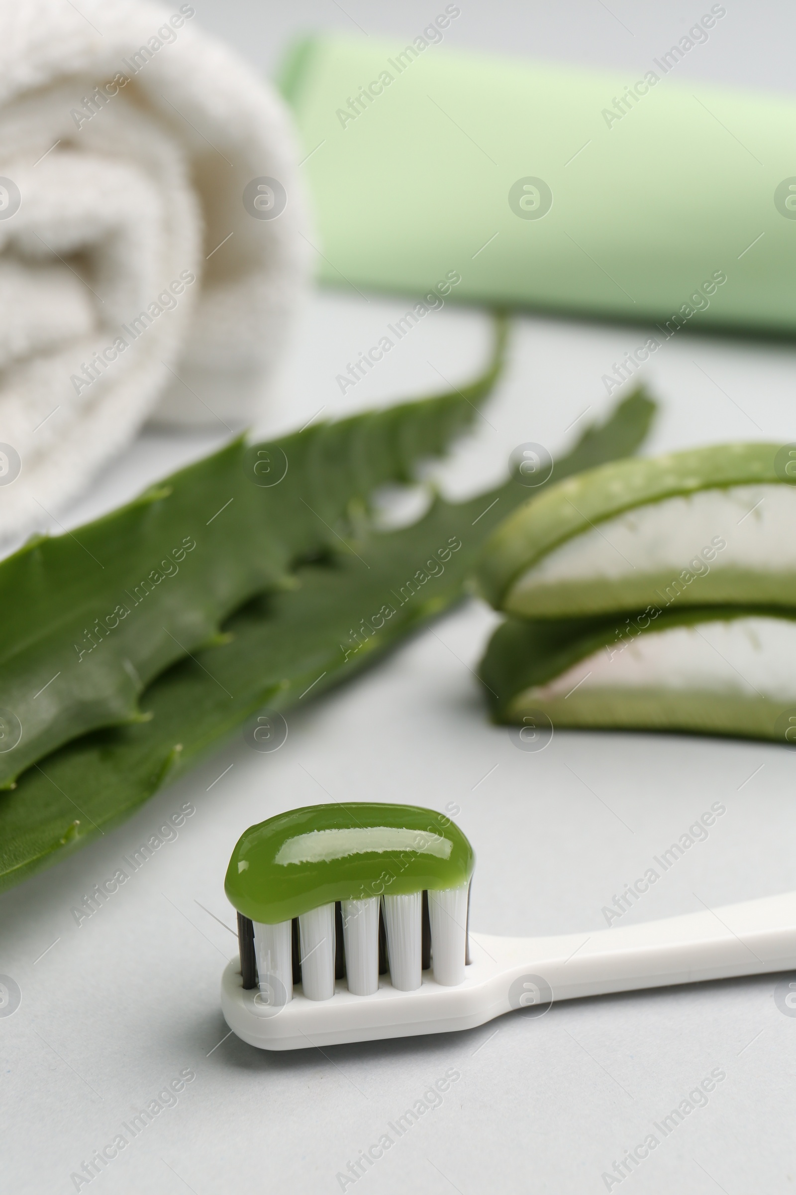 Photo of Toothbrush with toothpaste and fresh aloe on light grey background, closeup