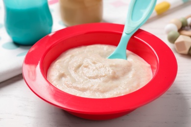 Photo of Healthy baby food in bowl on white wooden table, closeup