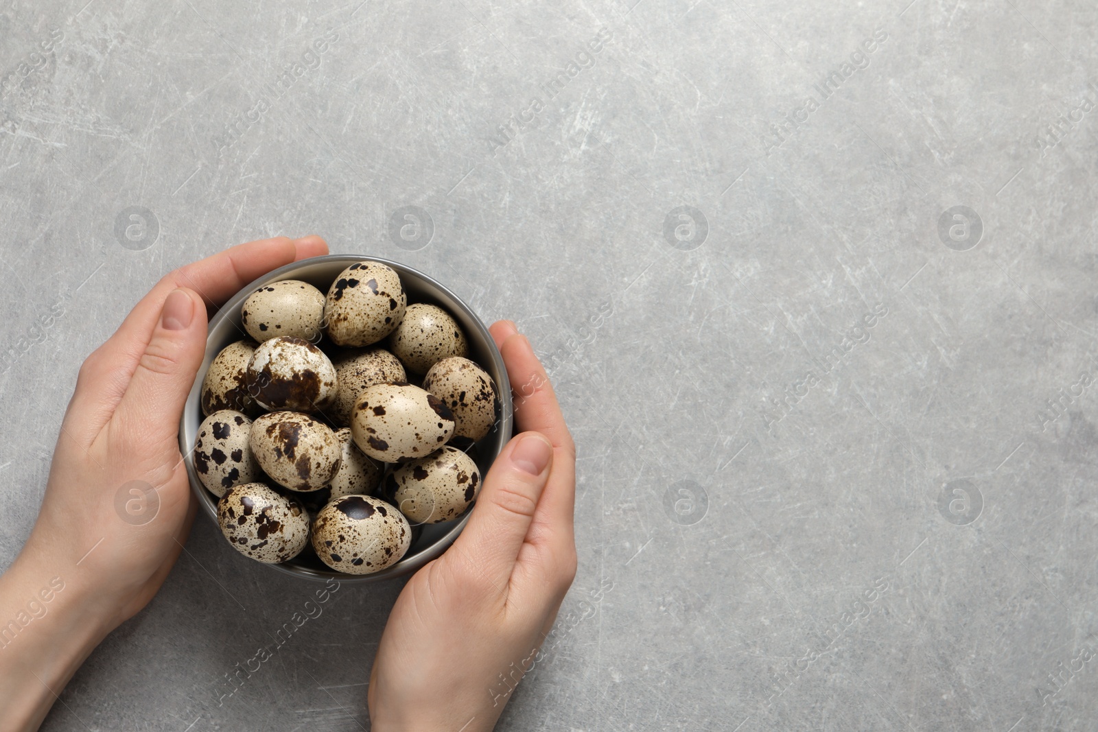 Photo of Woman holding bowl of quail eggs at light grey table, top view. Space for text