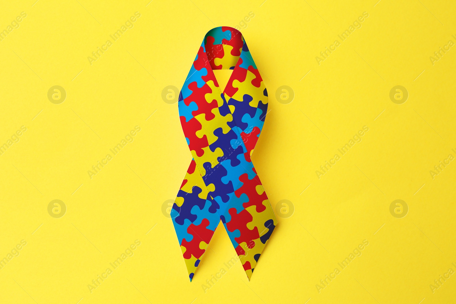 Image of World Autism Awareness Day. Colorful puzzle ribbon on yellow background, top view