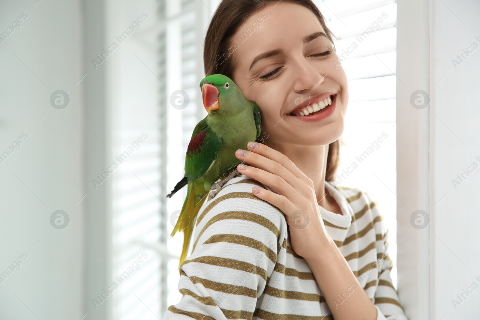 Photo of Young woman with cute Alexandrine parakeet indoors