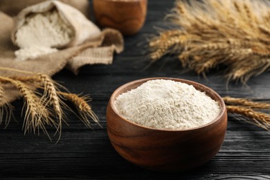 Bowl of flour and wheat ears on black wooden table