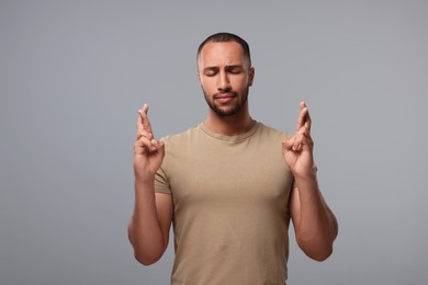 Young man crossing his fingers on grey background