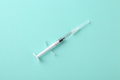 Photo of Injection cosmetology. One medical syringe on turquoise background, top view
