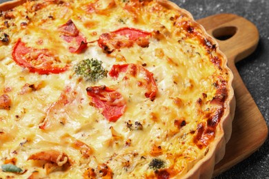 Tasty quiche with tomatoes and cheese on dark textured table, closeup