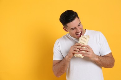 Man eating delicious shawarma on yellow background, space for text