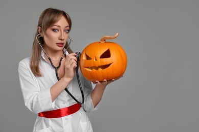 Woman in scary nurse costume with carved pumpkin and stethoscope on light grey background, space for text. Halloween celebration