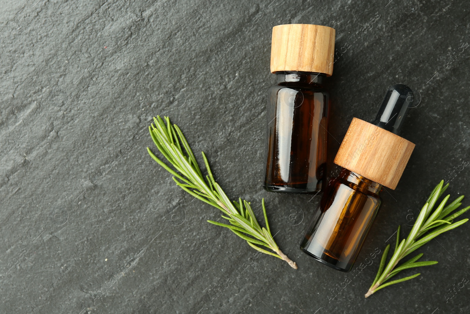 Photo of Essential oils in bottles and rosemary on gray textured table, flat lay. Space for text